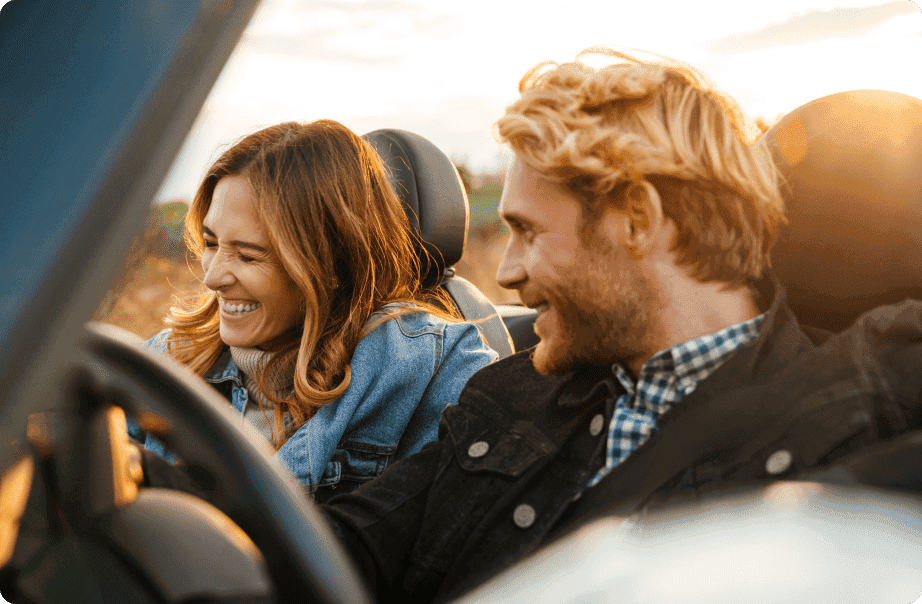 A couple driving a sports car with smiles on their faces A couple driving a sports car with smiles on their faces