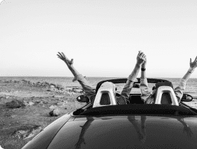 A couple celebrating while driving a convertible with their hands in the air A couple celebrating while driving a convertible with their hands in the air